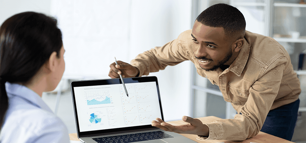 Um homem sorrindo mostrando gráficos para uma mulher que trabalha com ele, onde ambos trabalham na Total IP
